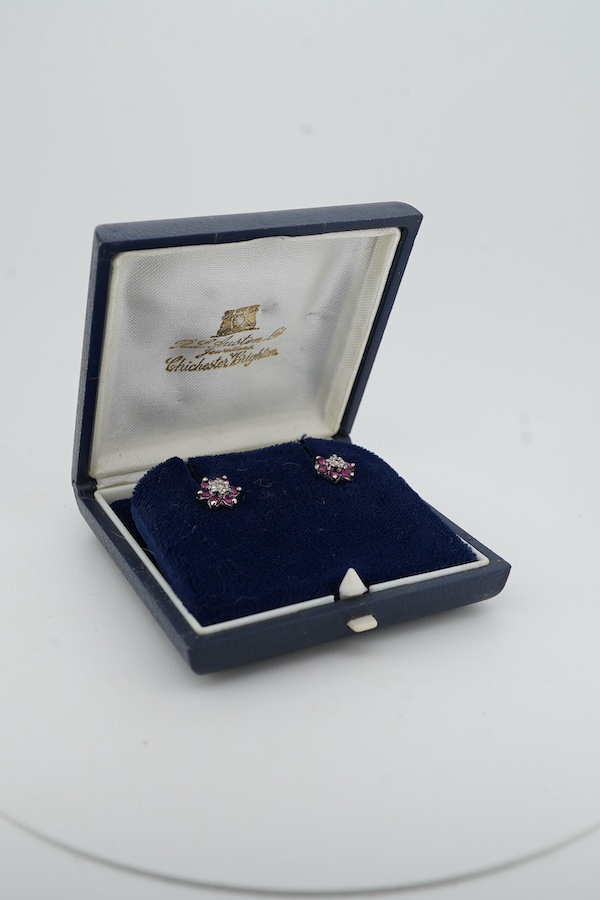 A pair of ruby and diamond stud earrings, of cluster design, set with a circular-cut rubies and single-cut diamonds, mounted in 9ct white gold, 8.5mm diameter each, post fittings, British hallmarks